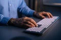 Close-up hands of unrecognizable man writing message to social network on wireless keyboard at night