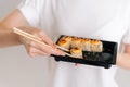 Close-up hands of unrecognizable young woman taking fresh sushi rolls with chopsticks on white isolated background in Royalty Free Stock Photo