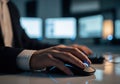 Close up of hands using a computer mouse in a dimly lit office with multiple monitors Royalty Free Stock Photo