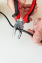 Close-up of hands using red and black pliers to cut a black cable on a white background. Royalty Free Stock Photo