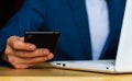 Close-up of the hands of a well-dressed man in a blue suit and a white shirt looking at his smartphone, using a laptop on a desk Royalty Free Stock Photo