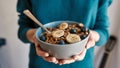 Close up of hands of woman holding homemade granola in a plate with nuts, honey, blueberries, banana and other natural