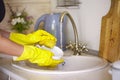 Close up hands of woman wearing yellow gloves washing dishes in kitchen Royalty Free Stock Photo