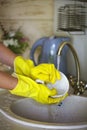 Close up hands of woman wearing yellow gloves washing dishes in kitchen Royalty Free Stock Photo