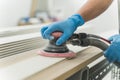 close-up hands of worker with gloves using electric sander in workshop. Joiner sanding wooden board on table. Carpentery