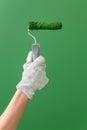 Close up of hands in working gloves holding middle-sized roller with green paint in front of green wall Royalty Free Stock Photo