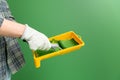 Close up of hands in working gloves holding yellow paint trough with middle-sized roller with green paint in front of green wall Royalty Free Stock Photo