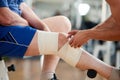 Close up hands wrapping bandage on male leg in gym.