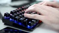 Close-up of hands writing on RBG mechanical keyboard during daytime with cellphone and glowing mouse in the background. Hacking in