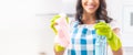 Close-up of hands in yellow rubber gloves holding a detergent and a cleaning rag by a smiling female blurred in teh back wearing Royalty Free Stock Photo