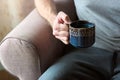 Close up of hands of young caucasian man holding a cup of tea. Enjoying serene morning with hot tea in his living room at home,