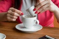 Close-up, hands of a young girl, pours cream or milk into coffee in a cafe on a wooden table