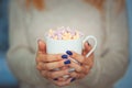 Close up hands of young woman female with manicure holding a cup of hot cocoa with marshmallow or coffee indoor near window on swe Royalty Free Stock Photo