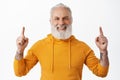 Close up of handsome hipster senior pointing fingers up and smiling happy. Old man with beard and tattoos showing