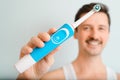 Close-up of handsome man with white toothy smile showing electric toothbrush, advertisement. Selective focus on modern device