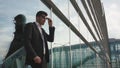 Close-up of handsome nervous businessman in glasses waiting for his retarded flight. Glass airport wall background