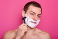 Close up of handsome shirtless man stands isolated over pink background. Guy with naked shoulders holds razor. Boy shaves and does