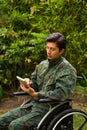 Close up of a handsome soldier sitting on wheel chair using his tablet with both hands, and wearing military uniform in