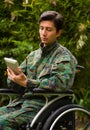 Close up of a handsome soldier sitting on wheel chair using his tablet with both hands, and wearing military uniform in