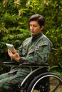 Close up of a handsome soldier sitting on wheel chair using his tablet with both hands, and wearing military uniform in