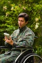 Close up of a handsome soldier sitting on wheel chair using his tablet with both hands, and wearing military uniform in