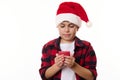 Close-up handsome teenage boy in Santa hat and red plaid shirt, makes cherished wish while holds a lit Christmas candle