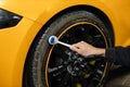 Close up of handsome young male employee worker cleaning the wheel tire of modern yellow sport car Royalty Free Stock Photo