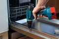 Close-up of a handyman repairing a dishwasher with an electric screwdriver Royalty Free Stock Photo