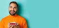 Close-up of happy adult man celebrating birthday, holding bday cake with candle and making wish, standing against