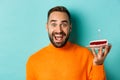 Close-up of happy adult man celebrating birthday, holding bday cake with candle and making wish, standing against