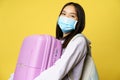 Close up of happy asian girl tourist in medical face mask, holding pink cute suitcase, going on vacation, travelling