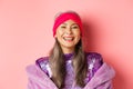 Close-up of happy asian senior lady in trendy purple outfit, laughing and smiling at camera, having fun on pink Royalty Free Stock Photo