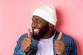 Close-up of happy Black bearded guy in beanie showing support, agree or approve something, giggle devious and showing