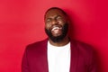 Close-up of happy and carefree Black man having fun, laughing and smiling, standing in blazer against red background Royalty Free Stock Photo