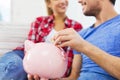 Close up of happy couple putting coin to piggybank