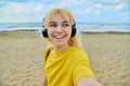 Close-up of happy face of teenage blonde in headphones on the beach.