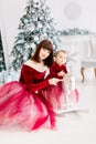 Close up of happy family, attractive mother and little girl, wearing red dresses, playing near Christmas tree at home Royalty Free Stock Photo