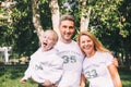 Close-up happy family in identical T-shirts with numbers and inscriptions - Family team, Mom, Dad - hugging in the park