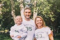 Close-up happy family in identical T-shirts with numbers and inscriptions - Family team, Mom, Dad - hugging in the park