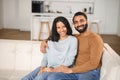 Close-up of happy couple looking at the camera while sitting at the sofa at their home. Happy owners of new flat smiling