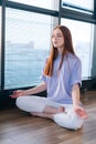 Close-up of happy relaxed young woman meditating sitting on floor in lotus pose on background of window in light office Royalty Free Stock Photo