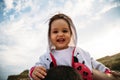 Close up of happy small baby girl in hood sitting on father`s shoulders on the sky background Royalty Free Stock Photo