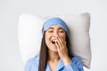 Close-up of happy smiling asian girl lying in bed on pillow wearing blue pajamas and sleeping eyemask, yawning satisfied Royalty Free Stock Photo