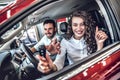 Close up of a happy young couple smiling showing car keys and thumbs up in a new car at the dealership Royalty Free Stock Photo