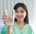 Close up of happy young inpatient woman who is getting well from her ailment smiling on to camera and holding a glass of water in