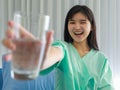 Close up of happy young inpatient woman who is getting well from her ailment smiling on to camera and holding a glass of water in