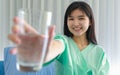 Close up of happy young inpatient woman who is getting well from her ailment smiling on to camera and holding a glass of water in