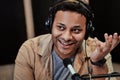 Close up of happy young male radio host smiling aside while broadcasting in studio, using microphone and headphones Royalty Free Stock Photo