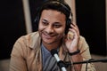 Close up of happy young male radio host smiling aside while broadcasting in studio, using microphone and headphones Royalty Free Stock Photo