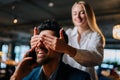 Close-up of happy young woman closed eyes of surprised elegant man in suit sitting at table talking on mobile phone in Royalty Free Stock Photo